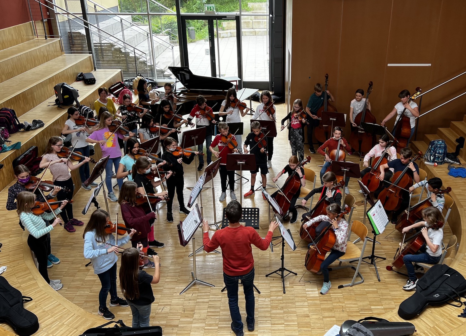 Streichinstrumente spielende Kinder mit Dirigent im Forum der Schule